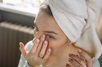 Adult woman applying under-eye masks at home for skincare routine.