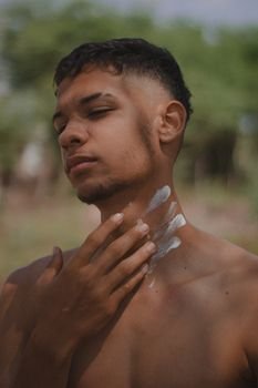 A young man applies sunscreen outdoors on a sunny summer day, showcasing skincare and sun protection.